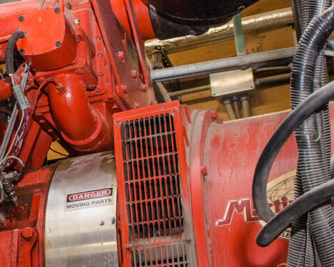 Rote industrielle Generator- oder Motoranlage mit Warnschild und Kabeln in einer Maschinenumgebung.