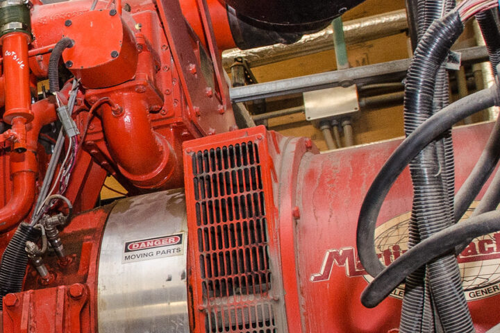 Rote industrielle Generator- oder Motoranlage mit Warnschild und Kabeln in einer Maschinenumgebung.