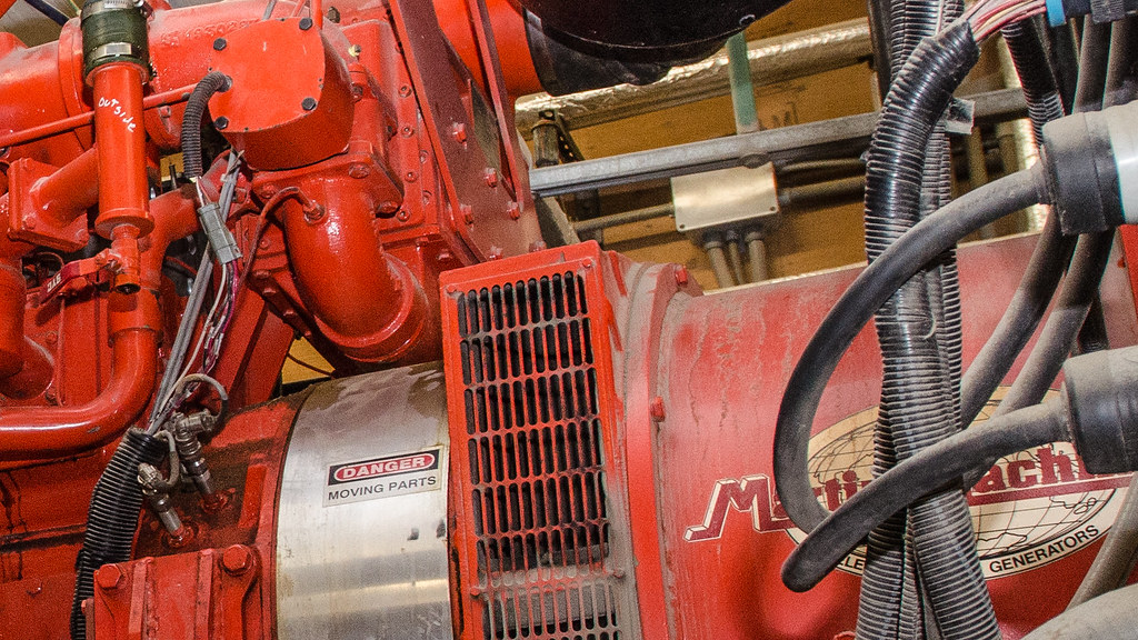 Rote industrielle Generator- oder Motoranlage mit Warnschild und Kabeln in einer Maschinenumgebung.
