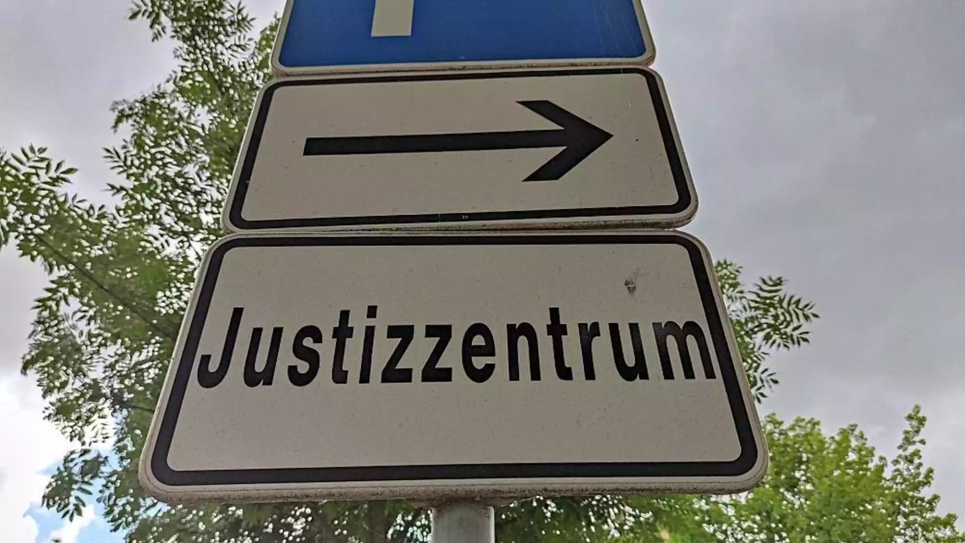 Radikale Töchter klagen in Köln gegen Bund wegen Förderstopp 1 Straßenschild mit Pfeil und der Aufschrift „Justizzentrum“ vor Bäumen und Himmel.