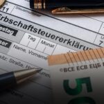 Nahaufnahme eines deutschen Formulars zur Erbschaftsteuer mit Münze, Stift und Euro-Banknoten.