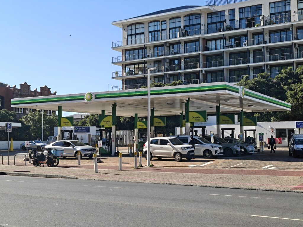 BP-Tankstelle mit mehreren Autos vor einem modernen Wohngebäude bei klarem Himmel.
