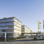 Moderne Bürogebäude auf einem Firmengelände mit mehreren Fahnen am Eingang.