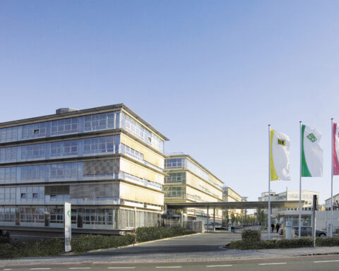 Moderne Bürogebäude auf einem Firmengelände mit mehreren Fahnen am Eingang.
