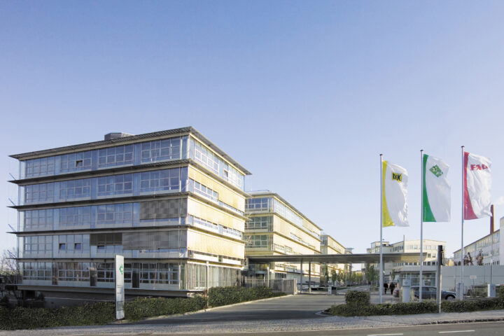 Moderne Bürogebäude auf einem Firmengelände mit mehreren Fahnen am Eingang.