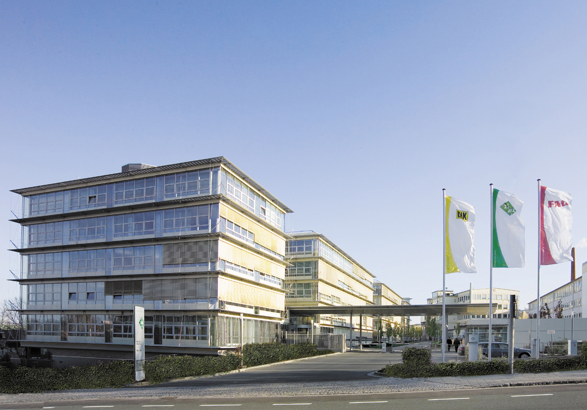 Moderne Bürogebäude auf einem Firmengelände mit mehreren Fahnen am Eingang.