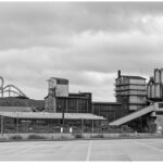 Industrieanlage mit Silos und Förderband unter bewölktem Himmel.