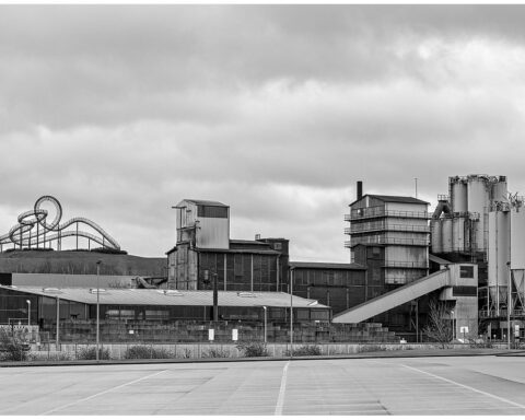 Industrieanlage mit Silos und Förderband unter bewölktem Himmel.
