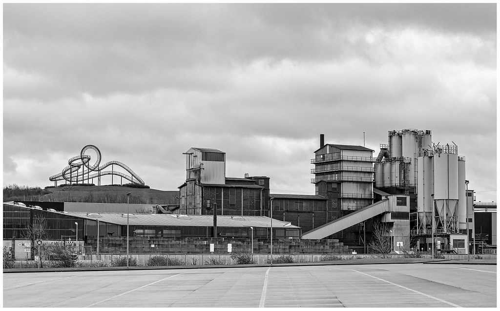 Industrieanlage mit Silos und Förderband unter bewölktem Himmel.