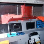 Blick in den Führerstand einer Vossloh-Lokomotive mit Bedienpult und roten Fahrzeugteilen.