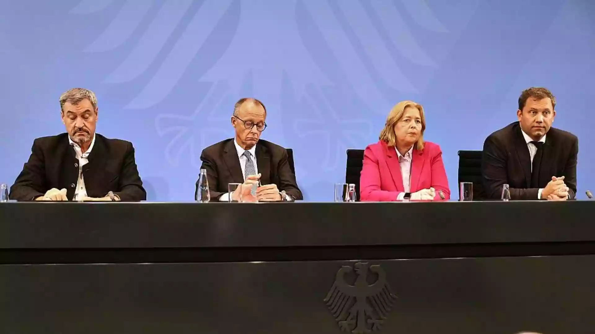 Vier Politiker sitzen an einem Konferenztisch vor blauem Hintergrund mit Bundesadler.