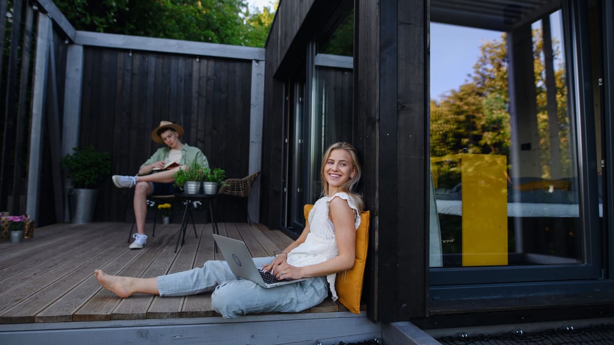 Tiny Houses unterliegen in Deutschland dem Baurecht und keiner eigenen Definition 1 Zwei Personen sitzen auf der Holzterrasse eines modernen Tiny Houses, eine Frau mit Laptop im Vordergrund.