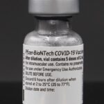 Eine Vial mit der Aufschrift Pfizer-BioNTech COVID-19 Vaccine vor dunklem Hintergrund.