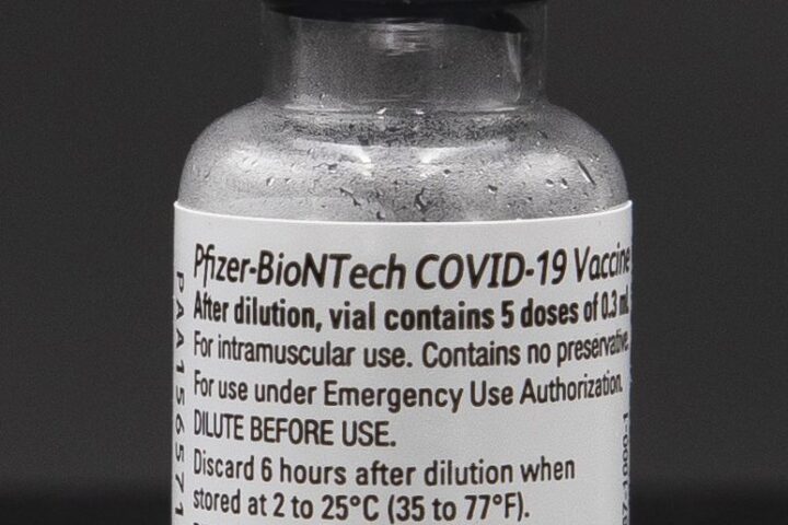 Eine Vial mit der Aufschrift Pfizer-BioNTech COVID-19 Vaccine vor dunklem Hintergrund.