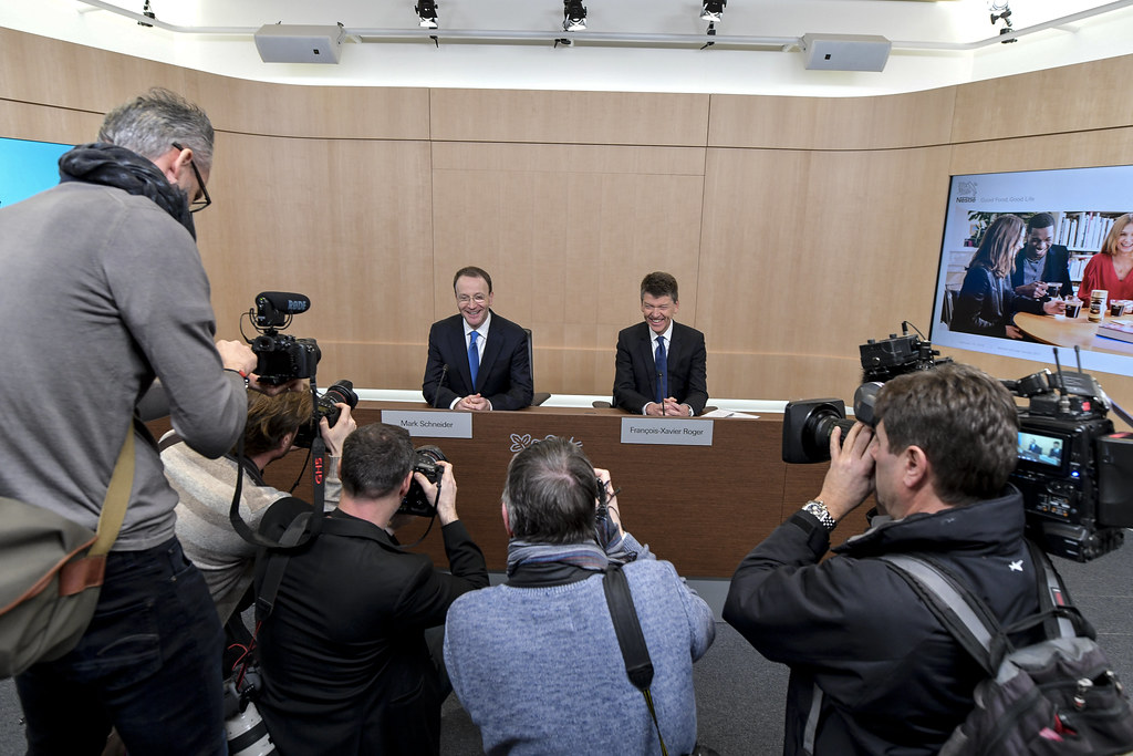 EU-Kommission genehmigt Nestlés Wassergeschäft-Deal mit Platinum Equity 1 Fotografen nehmen zwei Nestlé-Vertreter an einem Podium bei einer Presseveranstaltung auf.
