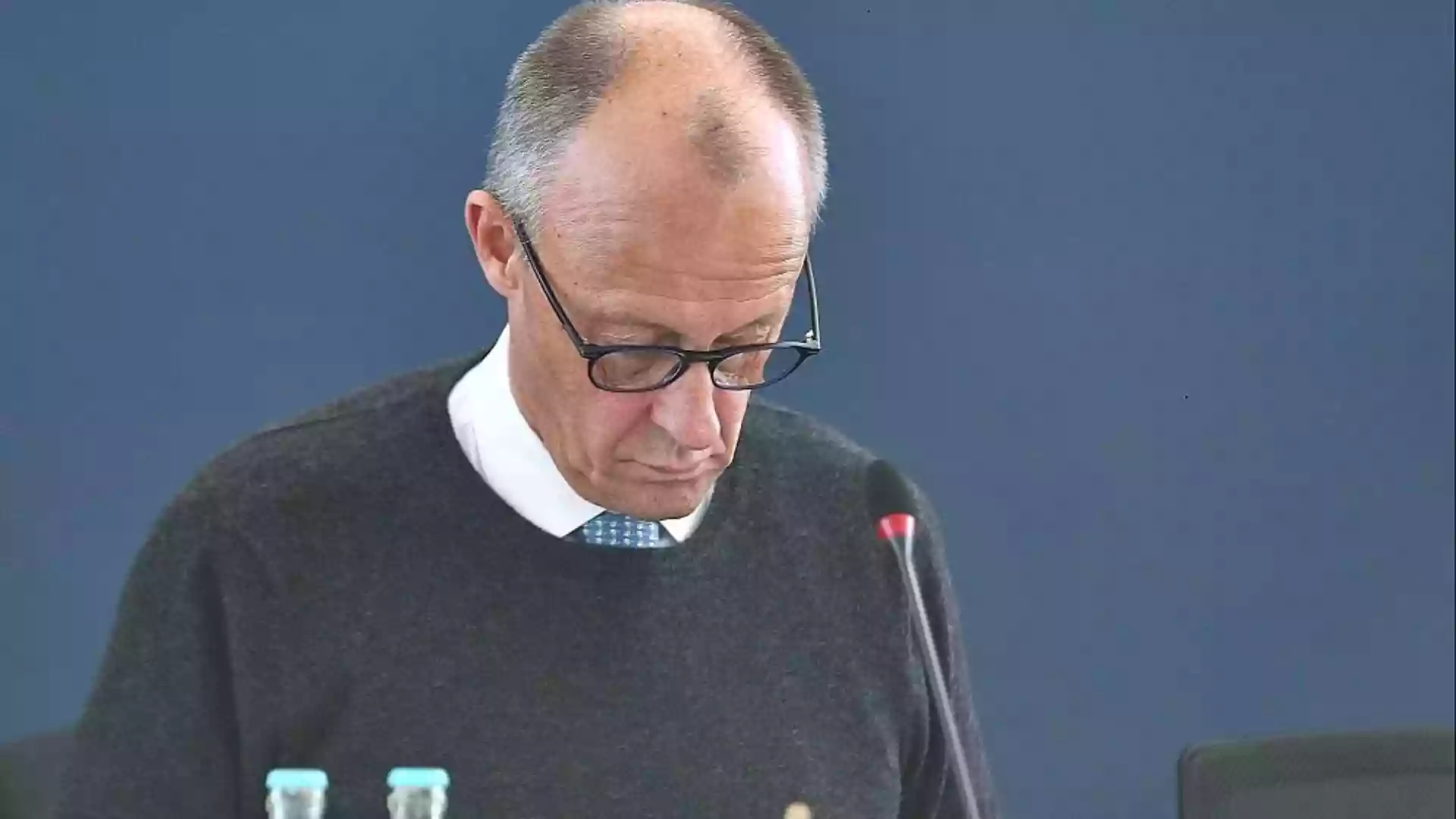 Friedrich Merz blickt bei einer politischen Sitzung nach unten, vor ihm steht ein Mikrofon.