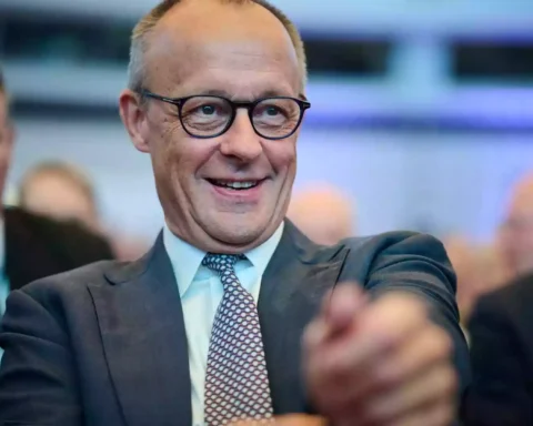 Alexander Schweitzer lächelt bei einer Veranstaltung im Innenraum, umgeben von weiteren Personen.