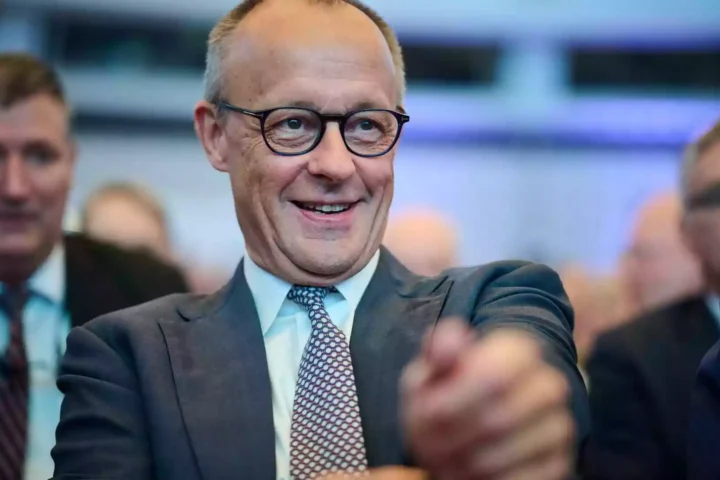 Alexander Schweitzer lächelt bei einer Veranstaltung im Innenraum, umgeben von weiteren Personen.