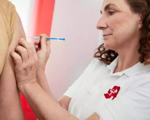 Eine Frau in weißem Poloshirt setzt einer Person eine Injektion in den Oberarm.
