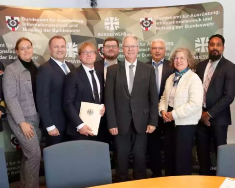 Gruppe von Personen posiert vor einem BAAINBw- und Bundeswehr-Hintergrundbanner in einem Besprechungsraum.