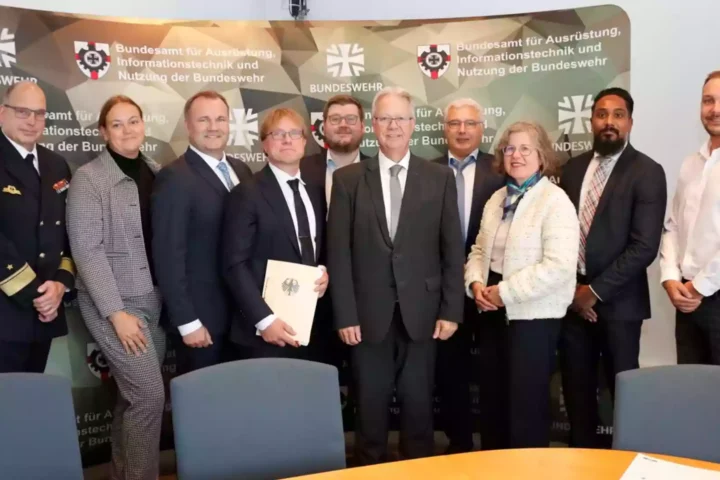 Gruppe von Personen posiert vor einem BAAINBw- und Bundeswehr-Hintergrundbanner in einem Besprechungsraum.