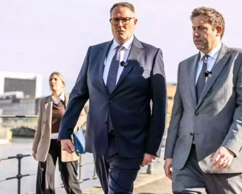 Alexander Schweitzer geht mit weiteren Personen im Freien entlang einer Uferpromenade.