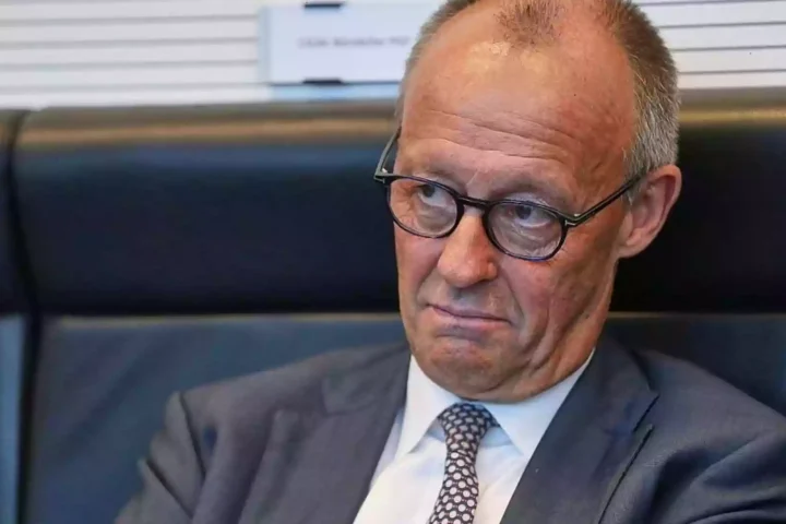 Friedrich Merz sitzt mit ernster Miene in einer Sitzung und blickt nach unten.