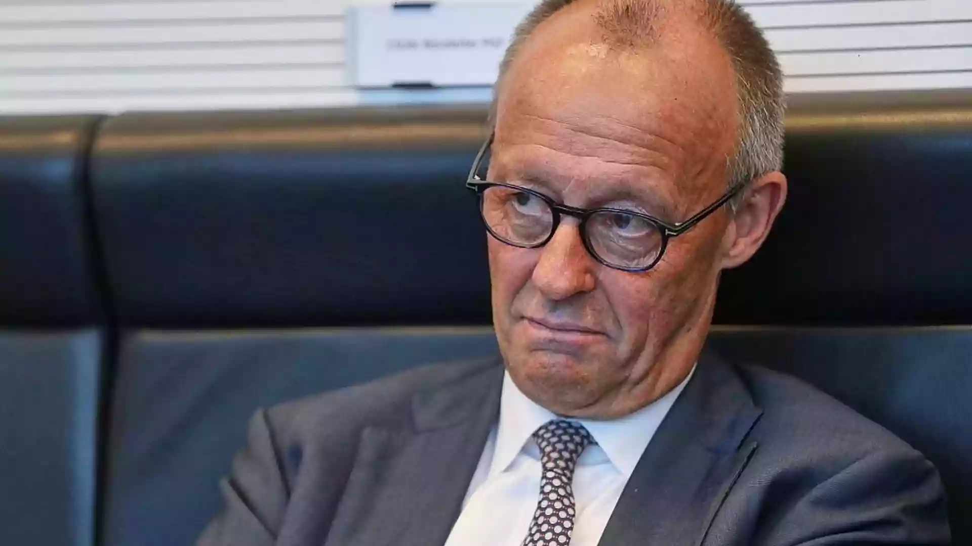 Friedrich Merz sitzt mit ernster Miene in einer Sitzung und blickt nach unten.