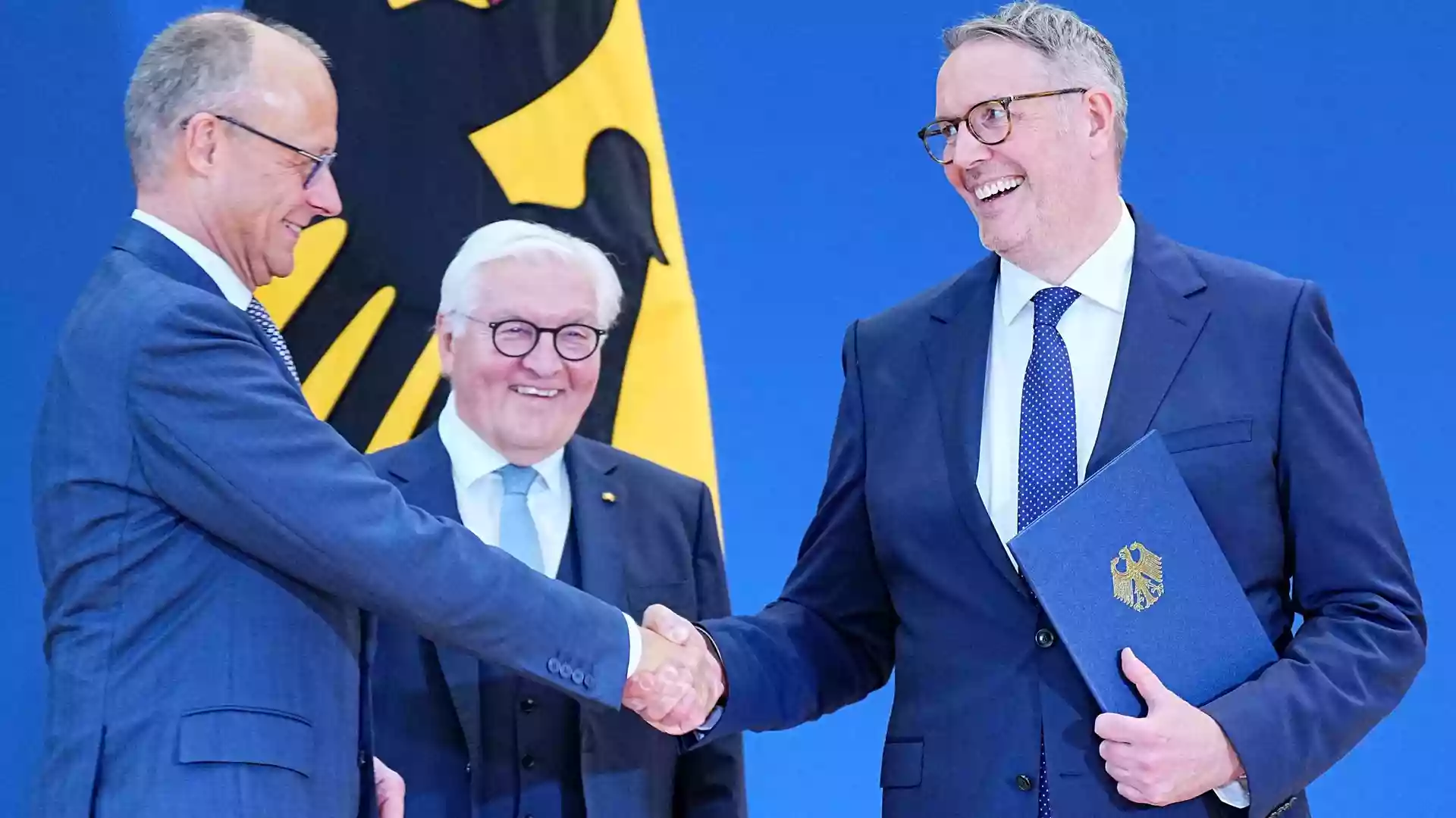 Alexander Schweitzer schüttelt in Berlin einem Mann im Anzug die Hand, während ein weiterer Politiker daneben lächelt.