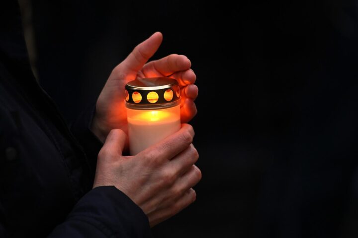 Hände halten eine brennende Kerze in dunkler Umgebung.