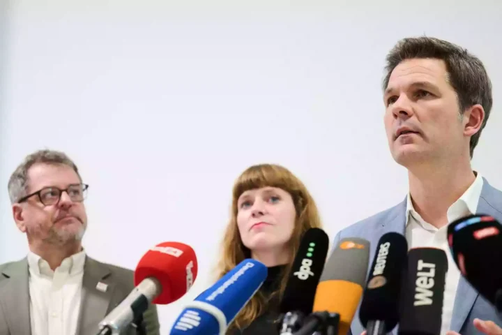 Drei Politiker stehen vor mehreren Mikrofonen bei einer Pressekonferenz.