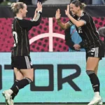 Zwei deutsche Fußballerinnen in schwarzen DFB-Trikots klatschen sich auf dem Spielfeld ab.