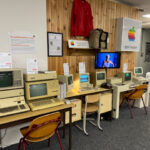 Ausstellung mit mehreren alten Apple-Computern und Apple-Logo an der Wand.