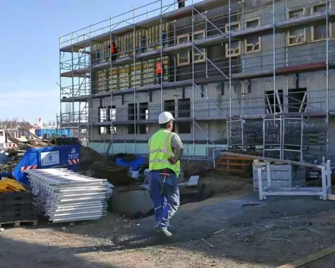 Bauarbeiter steht vor einem Wohngebäude im Bau mit Gerüst und Baumaterial auf der Baustelle.