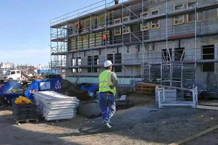 Bauarbeiter steht vor einem Wohngebäude im Bau mit Gerüst und Baumaterial auf der Baustelle.