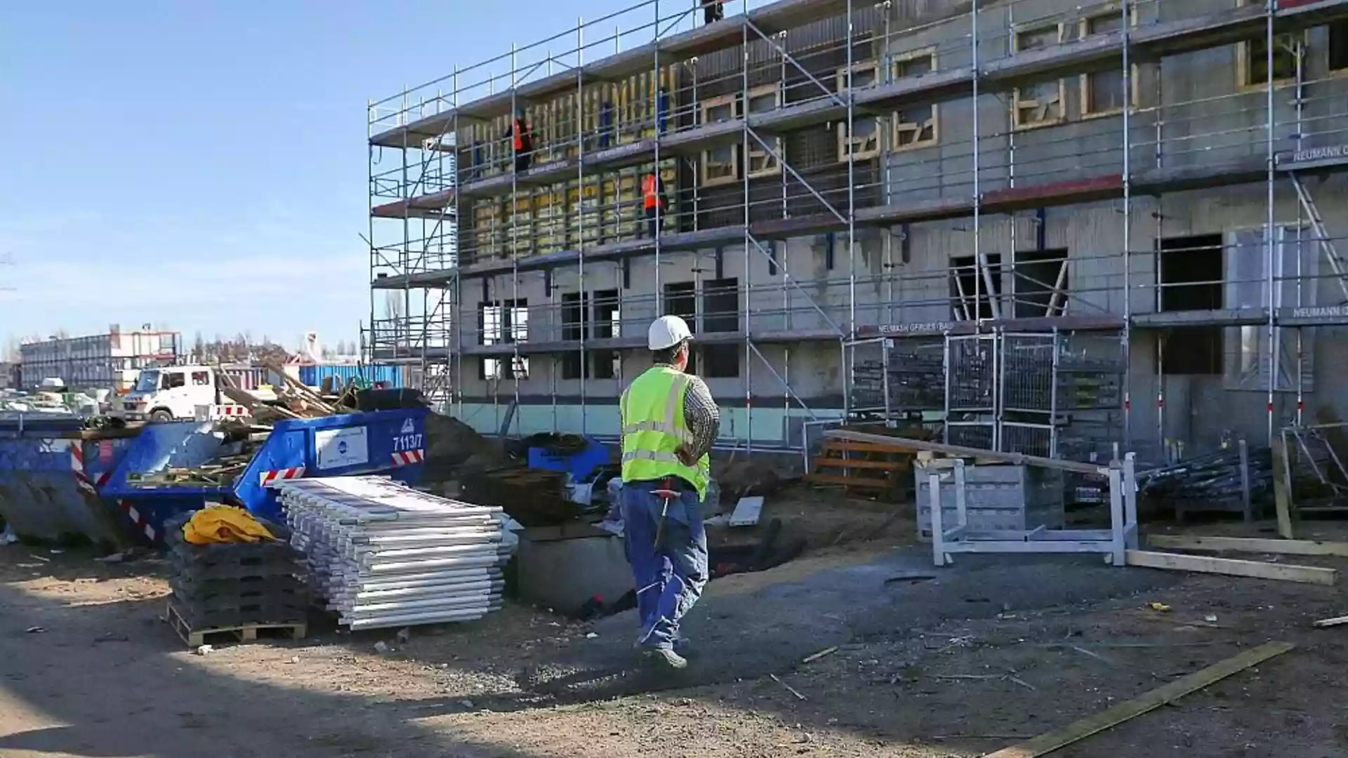 Bauarbeiter steht vor einem Wohngebäude im Bau mit Gerüst und Baumaterial auf der Baustelle.