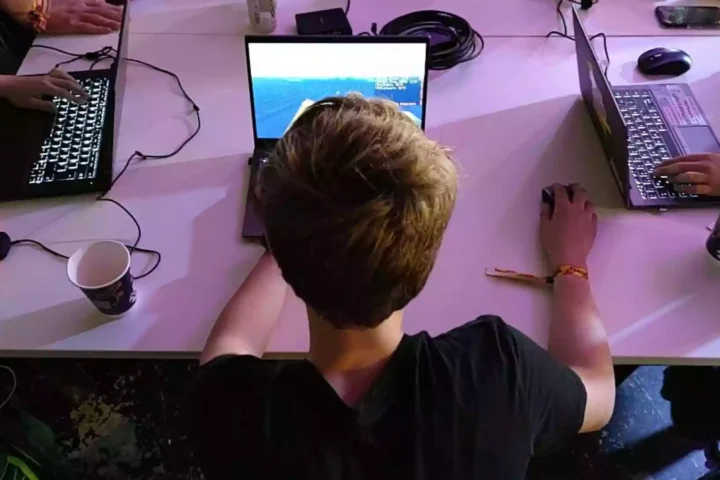 Jugendliche sitzen an Laptops an einem Tisch und nutzen Computer.
