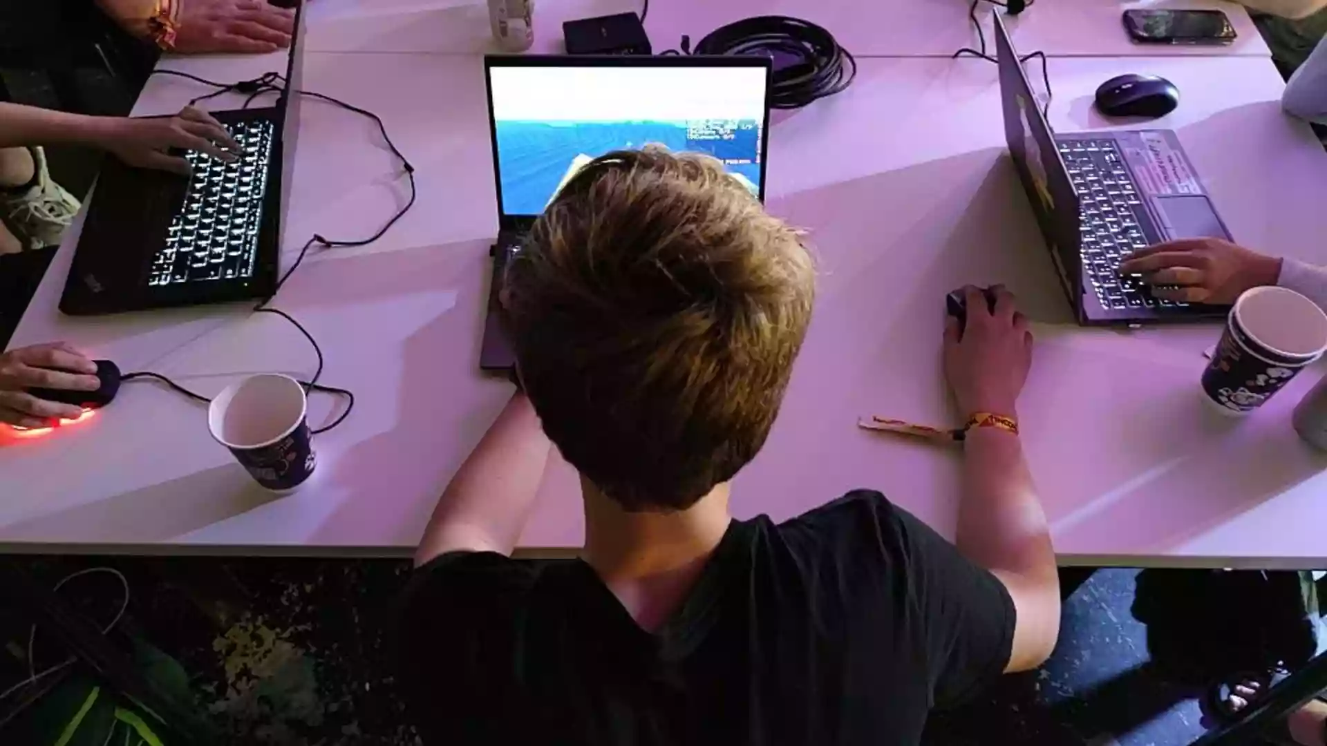 Jugendliche sitzen an Laptops an einem Tisch und nutzen Computer.