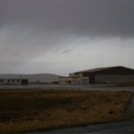 Ein Hangar und Nebengebäude auf einem Flughafen bei dunklem Himmel.