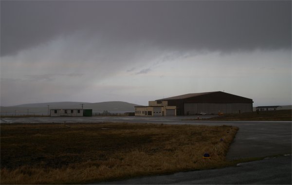 Ein Hangar und Nebengebäude auf einem Flughafen bei dunklem Himmel.