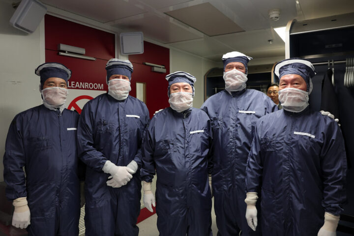 Fünf Personen in Reinraumanzügen stehen in einem Halbleiter-Reinraum vor einer Tür mit der Aufschrift „CLEANROOM“.
