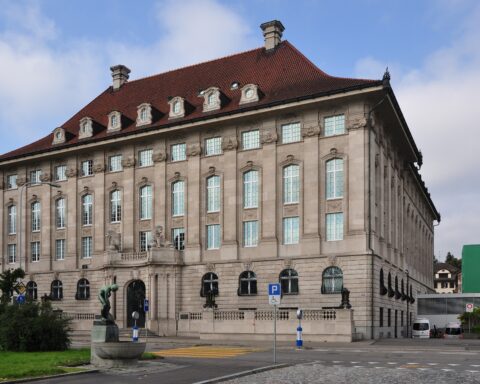 Außenansicht eines repräsentativen historischen Gebäudes mit rotem Ziegeldach unter blauem Himmel.