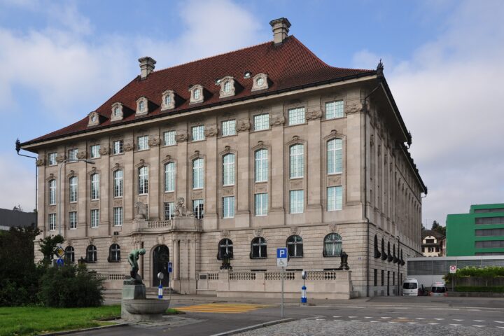 Außenansicht eines repräsentativen historischen Gebäudes mit rotem Ziegeldach unter blauem Himmel.
