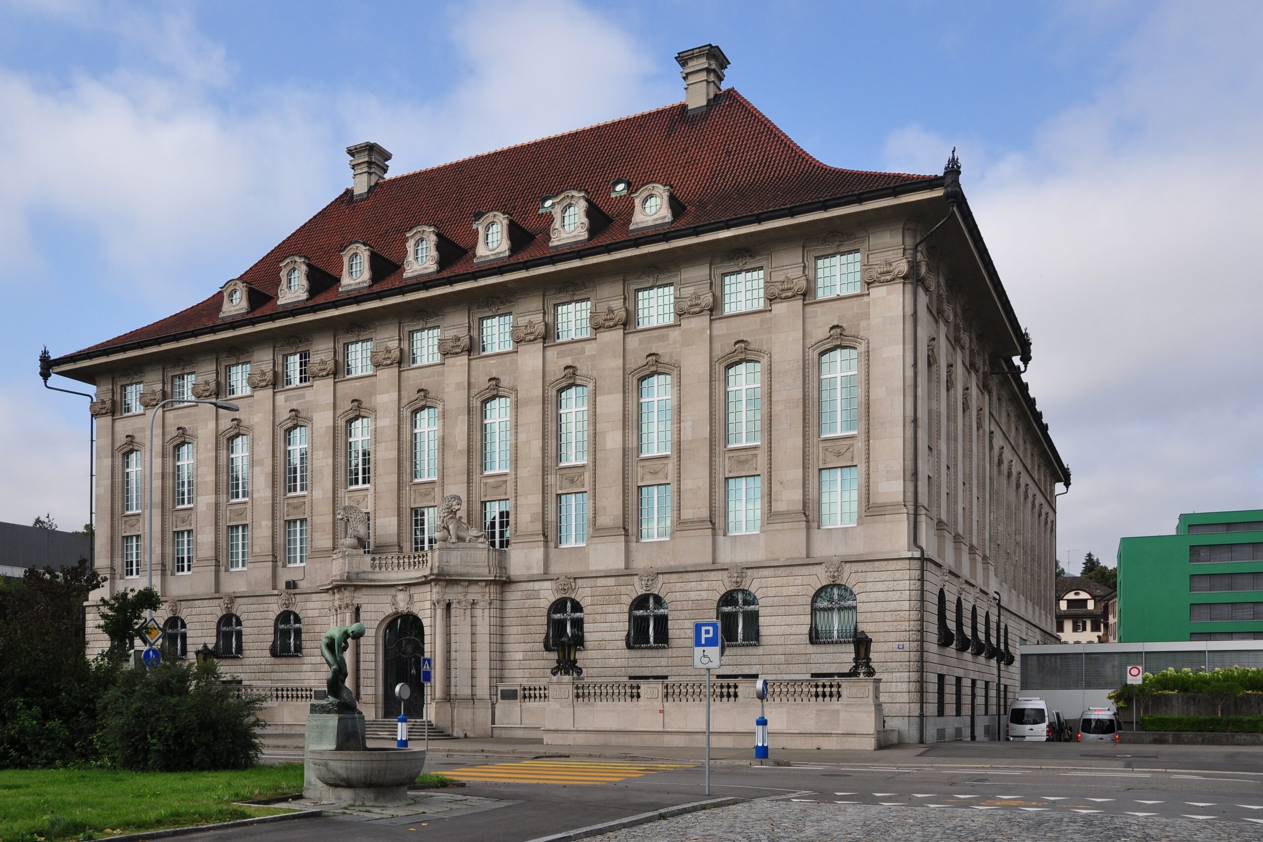 Außenansicht eines repräsentativen historischen Gebäudes mit rotem Ziegeldach unter blauem Himmel.