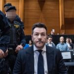 René Benko sitzt in einem Gerichtssaal, flankiert von Justizwachebeamten.