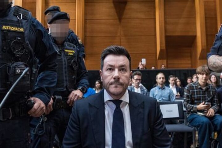 René Benko sitzt in einem Gerichtssaal, flankiert von Justizwachebeamten.