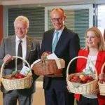Friedrich Merz steht mit mehreren Apfelköniginnen und hält einen Korb mit Äpfeln bei einem Empfang.