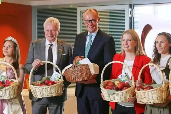 Friedrich Merz steht mit mehreren Apfelköniginnen und hält einen Korb mit Äpfeln bei einem Empfang.