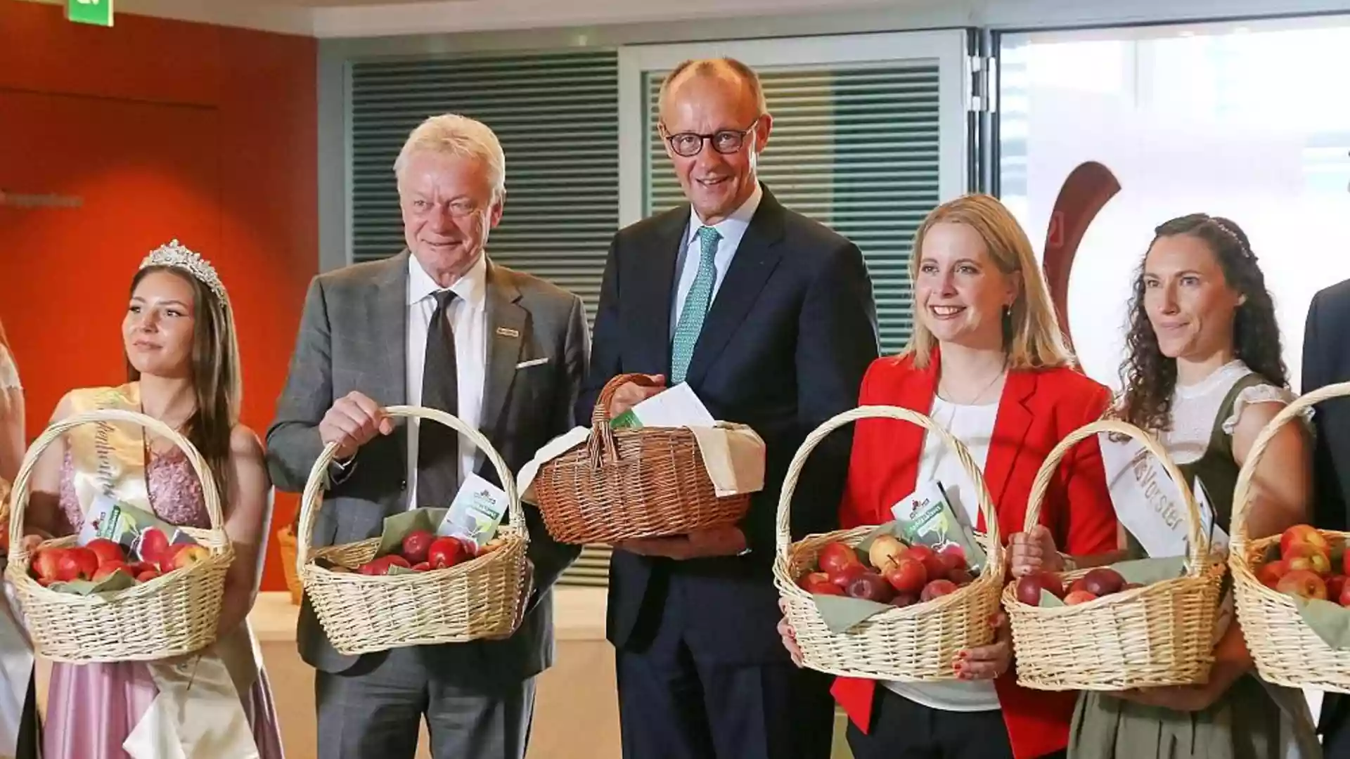 Friedrich Merz steht mit mehreren Apfelköniginnen und hält einen Korb mit Äpfeln bei einem Empfang.