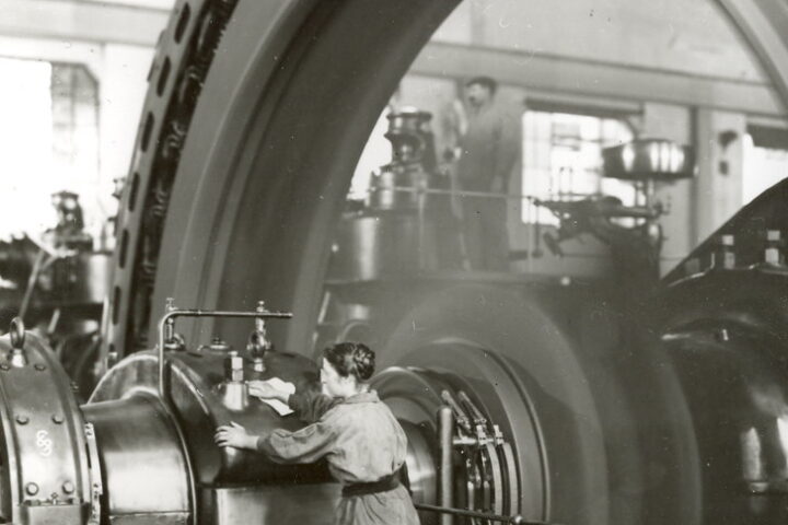 Arbeiter in einer Industrieanlage an einer großen Maschine im Innenraum.